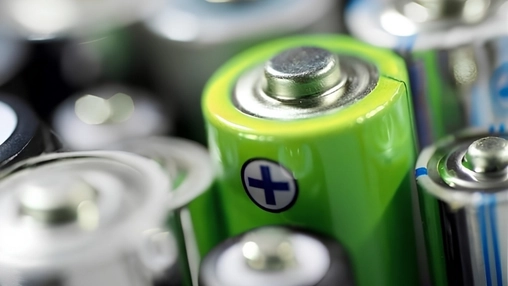 Group of green AA batteries with blue positive symbol stickers and metallic terminals in sharp focus