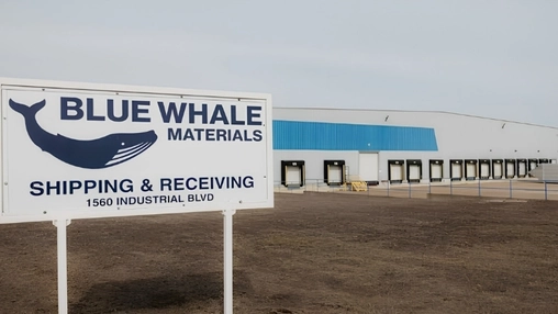 Blue Whale Materials facility sign in front of a large industrial warehouse with multiple loading dock doors