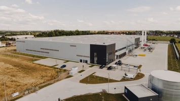 Aerial view of a large modern industrial facility with a grey warehouse building and surrounding access roads